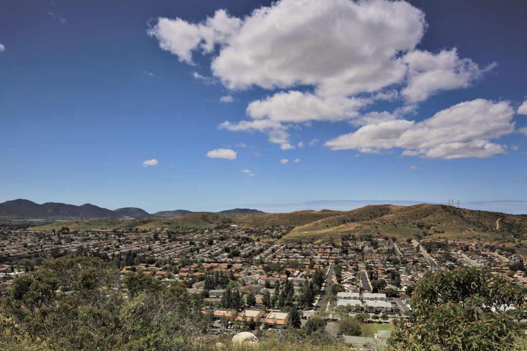 Aerial view of a residential neighborhood in San Diego, surrounded by rolling hills and a bright blue sky with scattered clouds